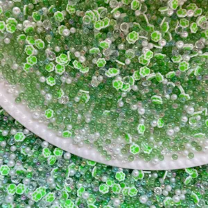 Close-up detail of mixed craft beads, including green cat paw clay slices, pearls and crystal beads.