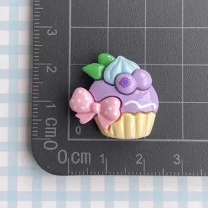 Resin purple cupcake cabochon charm with pink bow for DIY jewelry making and craft decor.