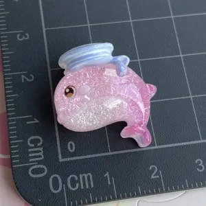 Nahaufnahme des rosa glitzernden Harz-Delfin-Charms mit Matrosenhut, ideal fuer DIY-Zubehoer.