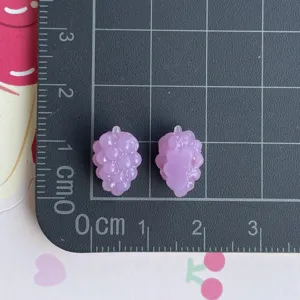Dettaglio del ciondolo in resina con uva viola in miniatura su tappetino graduato.