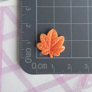 Detalle de dije de hoja de arce de resina naranja en estera de medida para manualidades.