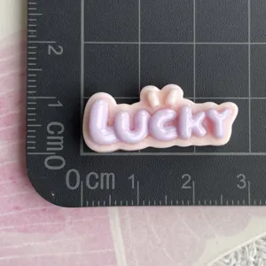 Primo piano dettagliato dell'accessorio artigianale in resina con lettera LUCKY viola e rosa.