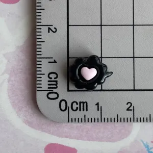 Close-up detail of a miniature black resin charm featuring a cute pink heart design.