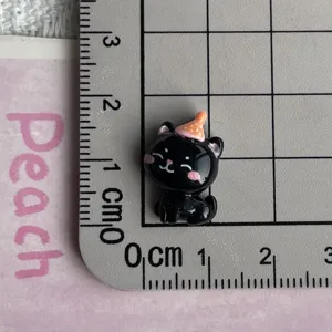 Close-up detail of cute mini black cat resin charm with party hat for DIY crafts.