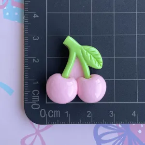 Close-up detail of cute pink cherry resin accessory with green leaves for DIY crafts.