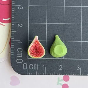 Dettaglio ravvicinato di ciondoli di fichi in resina in miniatura su tappetino a griglia.
