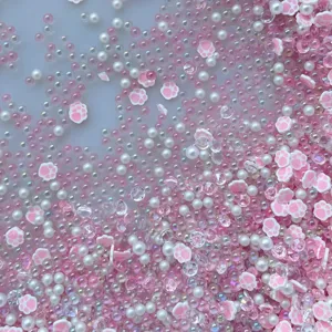 Close-up detail of mixed pink white pearl beads and cute cat paw charms for slime and DIY crafts.