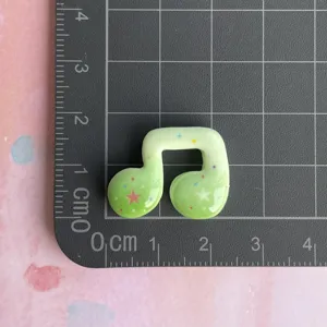 Close-up of green resin music note charm with colorful star patterns for DIY decor.