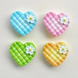 Nahaufnahme von bunten Mini-Gitterherz-Harz-Cabochons mit kleinen weißen Blumenanhängern.