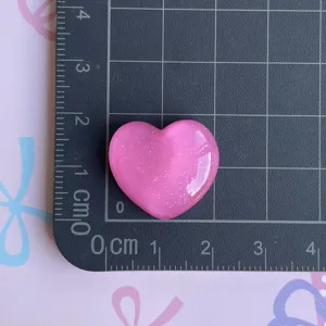 Detailed close-up of a sparkly pink heart resin cabochon accessory for DIY crafts and phone cases.