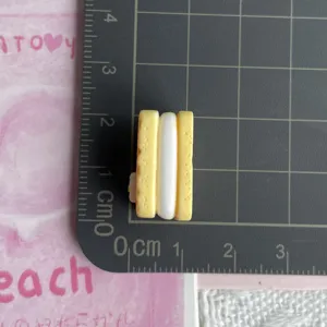 Detalle de dije de galleta sándwich amarilla de resina, muestra tamaño en alfombrilla.