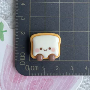 Resin bread cabochon detail view, cute smiley toast face design for DIY phone case craft accessories.