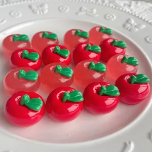 Dettaglio di ciondoli in resina a forma di mela rosa e rossa con foglie verdi ben definite.
