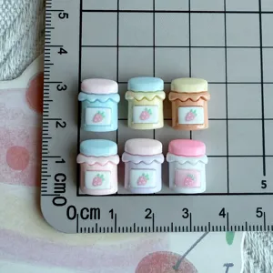 Miniature strawberry jam jar resin cabochons shown on a grid mat for scale detail.