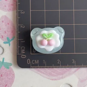 Close-up detail of glossy transparent resin bear charm with cherry cream cake design
