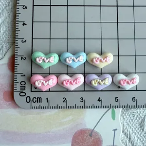 Close-up detail of colorful resin heart charms with love text, perfect for DIY nail art crafts.