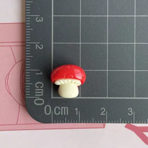 Vista dettagliata del mini ciondolo fungo rosso in resina per custodia telefono DIY.