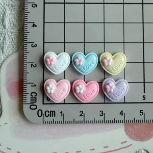 Mini resin heart cabochons with small flower and love text for DIY nail art crafts.