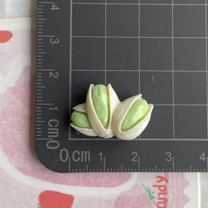 Gros plan du pendentif pistache en résine, détail de la taille sur tapis quadrillé, accessoire DIY.