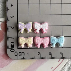 Close-up detail of mini resin bowknot charms with pretty embossed letters for nail art crafts.