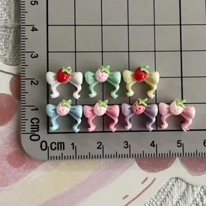 Detail view of colorful resin strawberry bow nail art charms and DIY jewelry accessories.