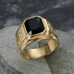 Macro view of men's gold ring with a large rectangular black gemstone and dragon texture