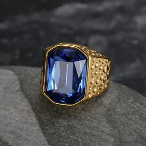 Close-up of gold men's ring with large blue zircon on textured rock