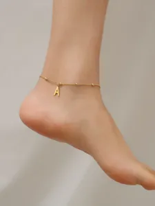 Macro view of an 18K gold titanium steel anklet with a hanging letter A charm.