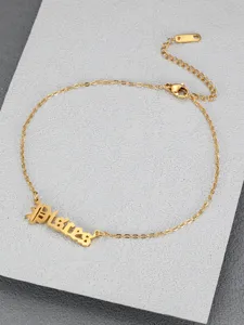 Macro detail of gold Pisces zodiac anklet in Old English font on textured gray surface