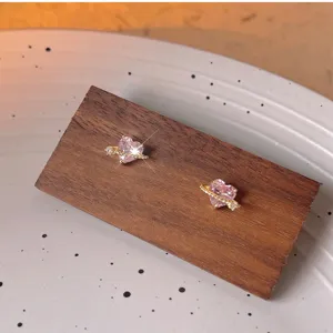 Detalle de pendientes de circonita con corazón rosa y planeta en soporte de madera, elegante.