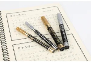 Close-up of gold and silver metallic signature markers resting on an open notebook page