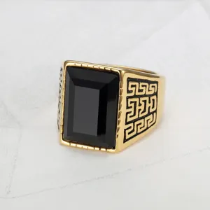 Close-up of a men's gold signet ring with a black gemstone and Greek key engraving