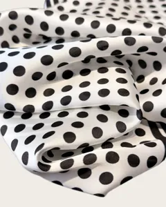 Close-up detail shot of classic black and white polka dot silk scarf fabric, smooth texture.
