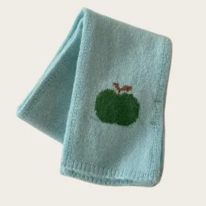 Close up of light blue knitted wool winter scarf featuring a cute green apple pattern detail.