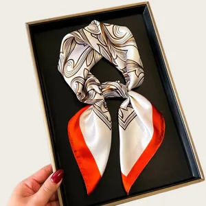 Close-up detail of white and brown abstract silk square scarf with vibrant orange border.