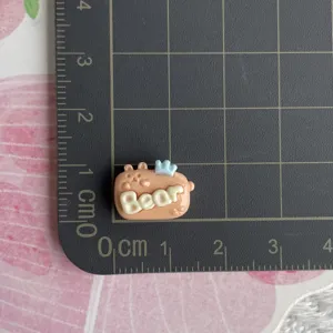 Close-up detail shot of a mini resin bear charm with letters and crown, perfect for DIY crafts.