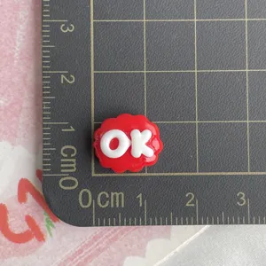Primo piano di un piccolo ciondolo con lettera OK in resina rossa per forcine fai da te e bricolage.