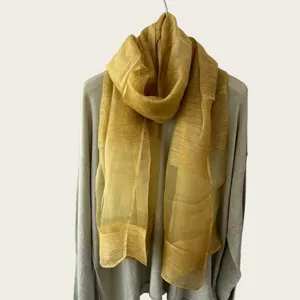 Vista detallada de una bufanda ligera y transparente amarillo mostaza sobre un suéter gris.