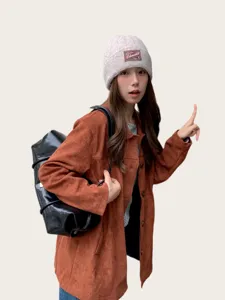 Detail view of a cozy gray knit beanie worn by a model with a stylish brown suede jacket.