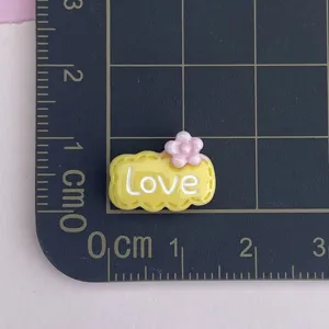 Mini resin charm detail shot showing size, yellow cloud design with love text and pink flower.