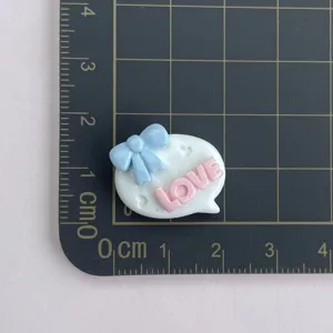 Gros plan du charm bulle en résine avec nœud bleu et lettres roses pour vos loisirs créatifs.