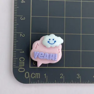 Détail du charm en résine bulle de parole rose avec texte YEAH et nuage souriant mignon.