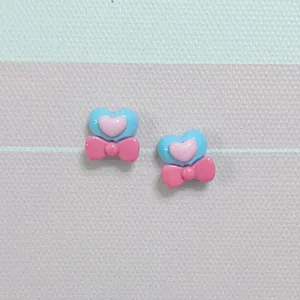 Close-up detail shot of cute blue and pink heart resin bow charms for nail art and DIY crafts.