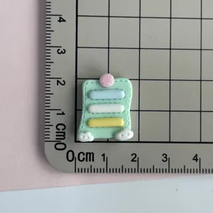 Detalle del dije de nota adhesiva de resina con tamaño compacto para fundas y accesorios de cabello.