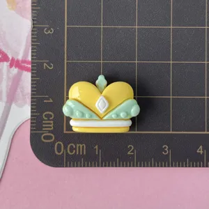 Detailed close-up of glossy yellow green crown resin cabochon charm for DIY crafts.