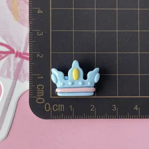 Close-up of a glossy blue crown resin accessory with pink and yellow details on a grid mat.