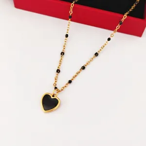 Close-up of gold stainless steel necklace with black enamel heart pendant and station beads.