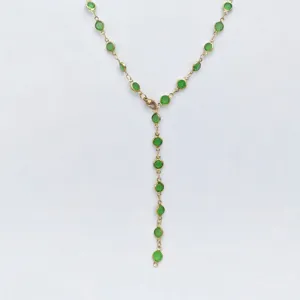 Closeup detail of the golden Y-chain necklace featuring bezel-set green glass stones.