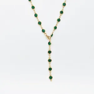 Detail shot of a stainless steel gold Y-shaped necklace featuring green bezel-set stones.