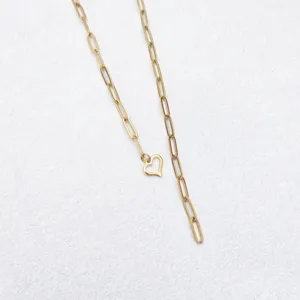 Close-up detail shot of a gold paperclip chain necklace featuring a delicate heart pendant.